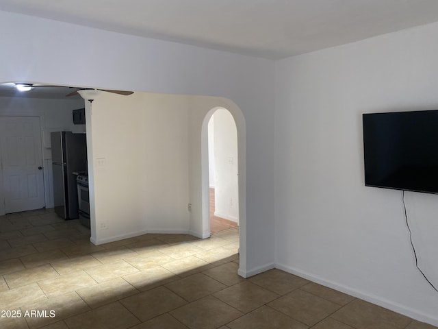 unfurnished room featuring arched walkways, tile patterned flooring, and baseboards