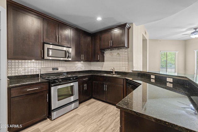 kitchen featuring light wood-style floors, a sink, dark stone countertops, and stainless steel appliances
