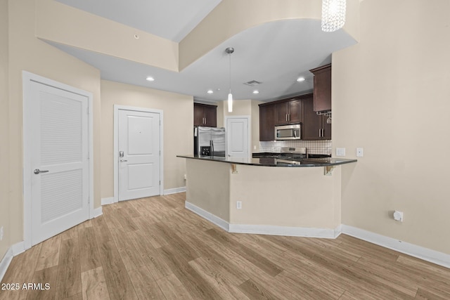 kitchen with dark brown cabinets, dark countertops, appliances with stainless steel finishes, light wood-style floors, and backsplash