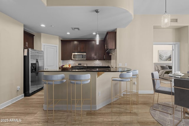 kitchen with visible vents, a peninsula, dark countertops, light wood-style floors, and stainless steel appliances