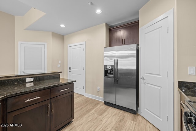 kitchen with dark brown cabinetry, stove, light wood finished floors, stainless steel fridge, and dark stone counters