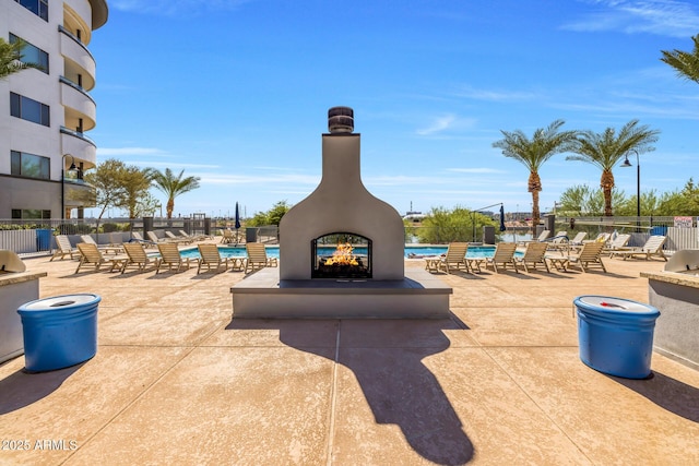 view of patio with fence, a community pool, and a multi sided fireplace