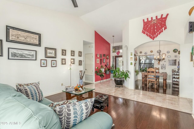 living room featuring baseboards, arched walkways, wood finished floors, an inviting chandelier, and vaulted ceiling