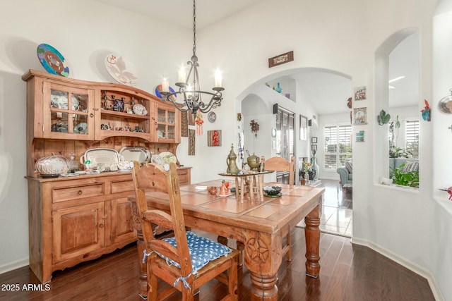 dining room featuring arched walkways, dark wood-style flooring, a chandelier, and baseboards