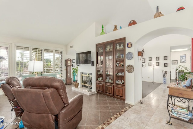 tiled living room with high vaulted ceiling, arched walkways, and a glass covered fireplace