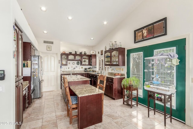 kitchen with a center island, visible vents, glass insert cabinets, a sink, and a kitchen bar