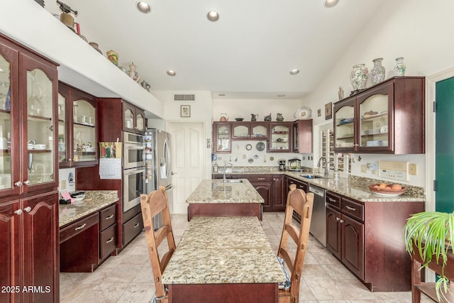 kitchen featuring stainless steel appliances, a sink, visible vents, a kitchen island, and glass insert cabinets