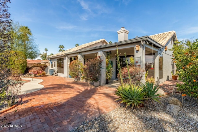 back of house featuring a tile roof, a chimney, stucco siding, a patio area, and fence