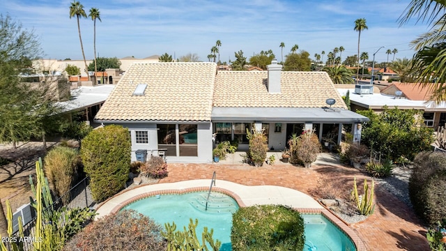 rear view of property featuring a patio, fence, a tiled roof, an outdoor pool, and a chimney