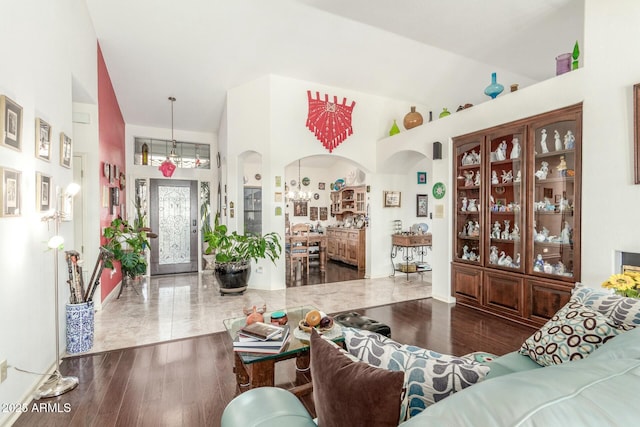 living room with arched walkways, a notable chandelier, lofted ceiling, and wood finished floors