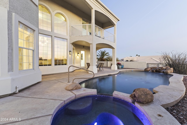 pool at dusk with an in ground hot tub and a patio