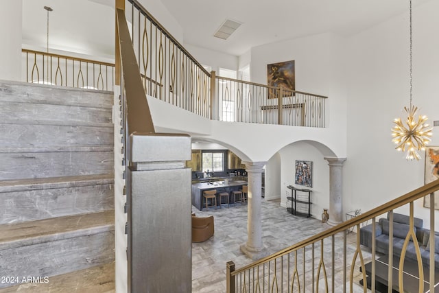 stairway featuring a towering ceiling, decorative columns, and an inviting chandelier