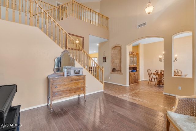 foyer with stairway, wood finished floors, baseboards, visible vents, and arched walkways