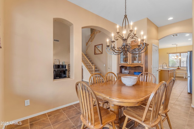 dining room with arched walkways, an inviting chandelier, light tile patterned floors, baseboards, and stairs