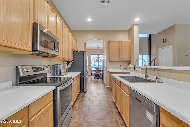 kitchen featuring arched walkways, a sink, light brown cabinetry, light countertops, and stainless steel appliances