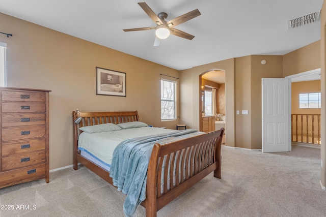 bedroom featuring baseboards, visible vents, ensuite bath, arched walkways, and light colored carpet