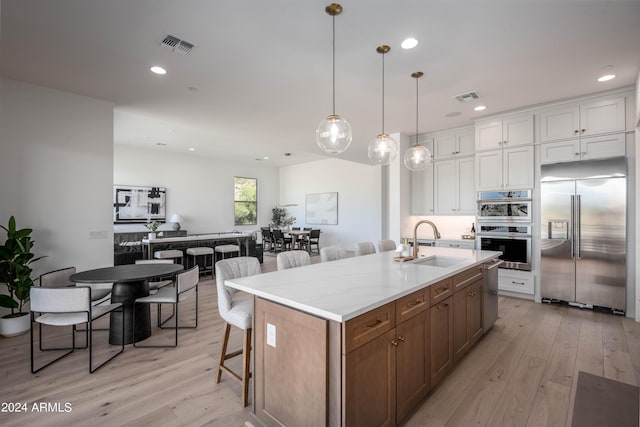 kitchen featuring sink, light hardwood / wood-style floors, a kitchen island with sink, white cabinets, and appliances with stainless steel finishes