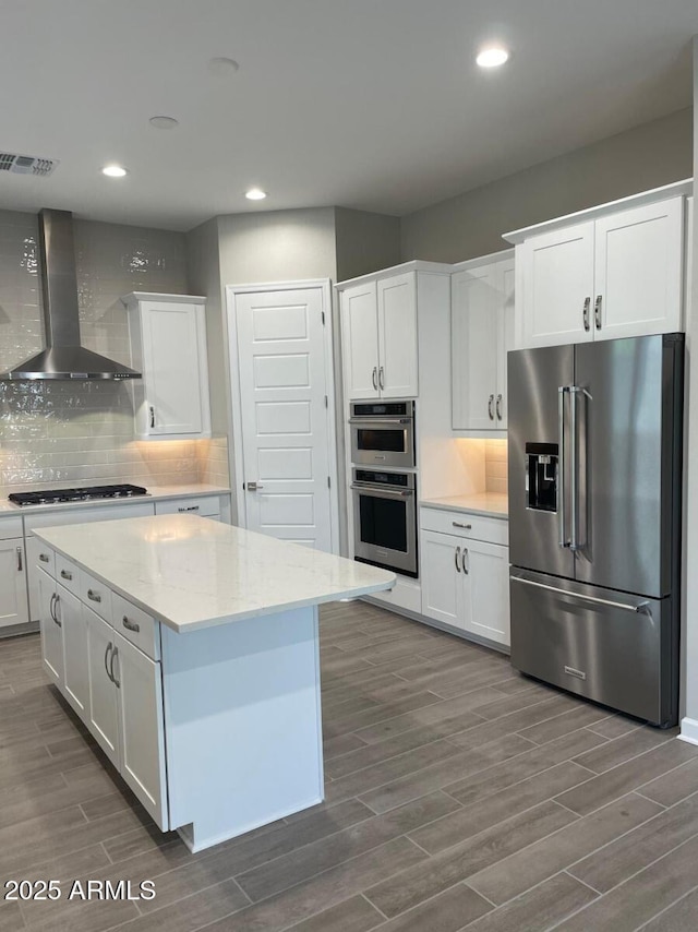 kitchen with backsplash, wall chimney range hood, wood tiled floor, stainless steel appliances, and white cabinetry