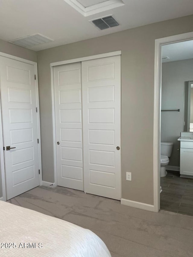 bedroom with visible vents, connected bathroom, baseboards, carpet flooring, and a closet