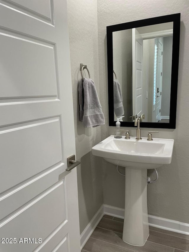 bathroom featuring a sink, baseboards, wood tiled floor, and a textured wall