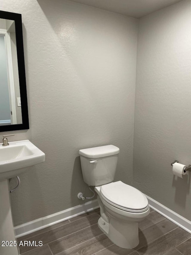 half bath featuring toilet, a textured wall, baseboards, and wood tiled floor