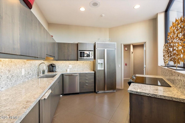 kitchen featuring decorative backsplash, light stone counters, built in appliances, and a sink