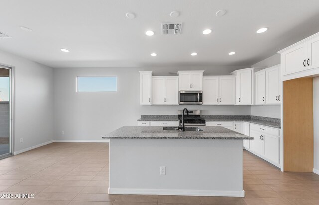 kitchen with white cabinetry, appliances with stainless steel finishes, a kitchen island with sink, and dark stone counters