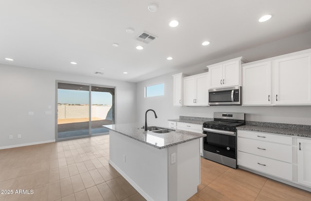 kitchen with sink, white cabinets, stainless steel appliances, light stone countertops, and a center island with sink