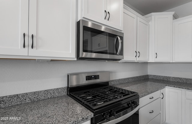 kitchen featuring white cabinetry, stainless steel appliances, and dark stone countertops