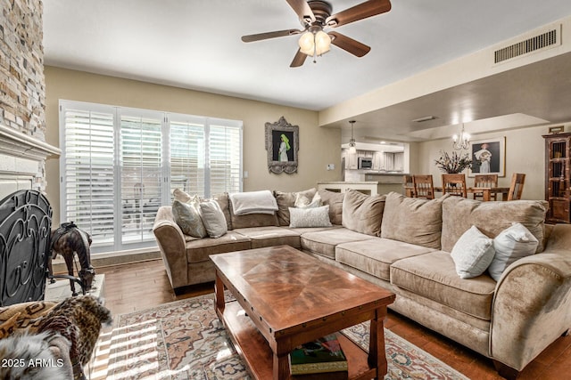 living area featuring a large fireplace, wood finished floors, visible vents, and a ceiling fan