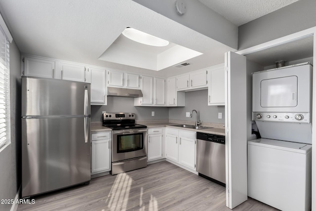 kitchen with stainless steel appliances, stacked washer and clothes dryer, white cabinets, and sink