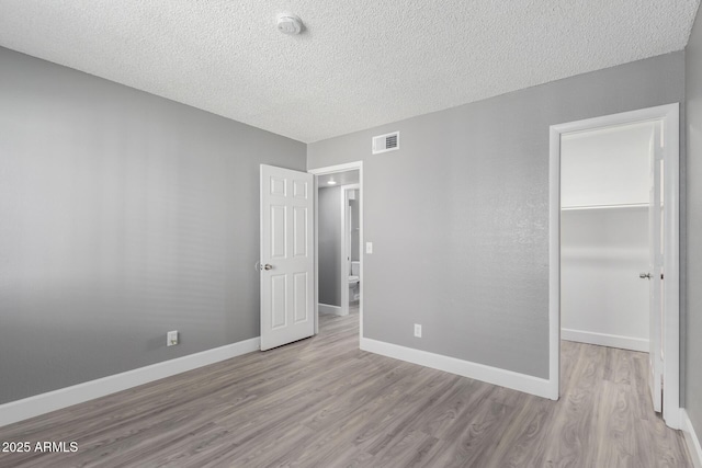 unfurnished bedroom with a spacious closet, a textured ceiling, a closet, and light wood-type flooring