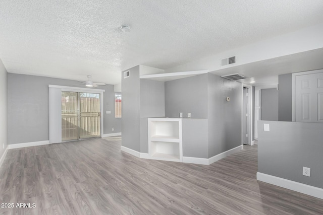 empty room featuring wood-type flooring, a textured ceiling, built in features, and ceiling fan