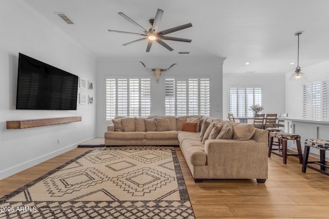 living area featuring ornamental molding, visible vents, light wood-style flooring, and a ceiling fan