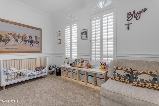 bedroom featuring ornamental molding, a wainscoted wall, carpet floors, a nursery area, and a decorative wall