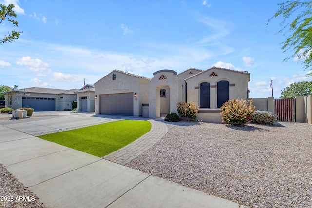 mediterranean / spanish-style house with concrete driveway, stucco siding, an attached garage, a tiled roof, and fence