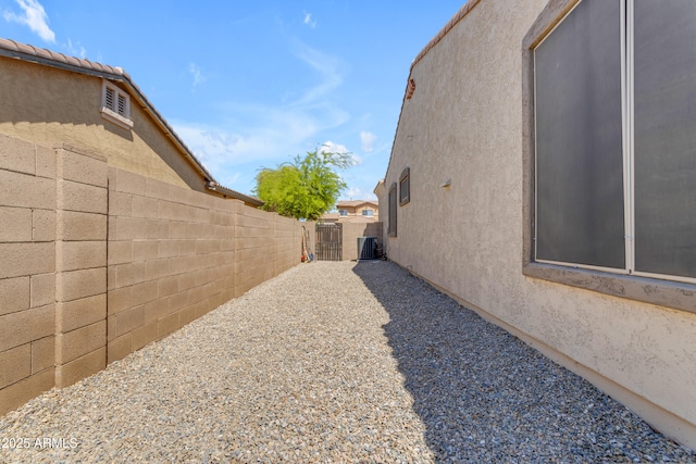 view of side of home featuring fence, cooling unit, a gate, and stucco siding