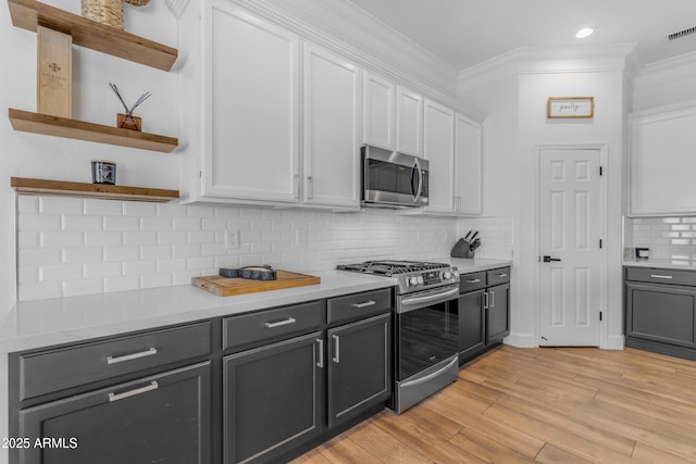 kitchen with ornamental molding, open shelves, white cabinets, appliances with stainless steel finishes, and light wood finished floors