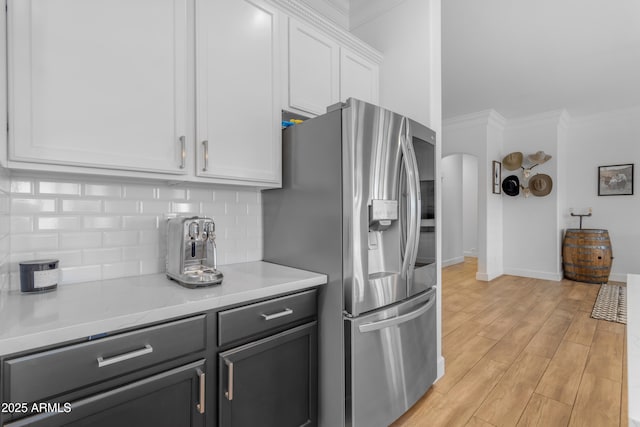 kitchen with stainless steel fridge with ice dispenser, arched walkways, light countertops, white cabinetry, and decorative backsplash