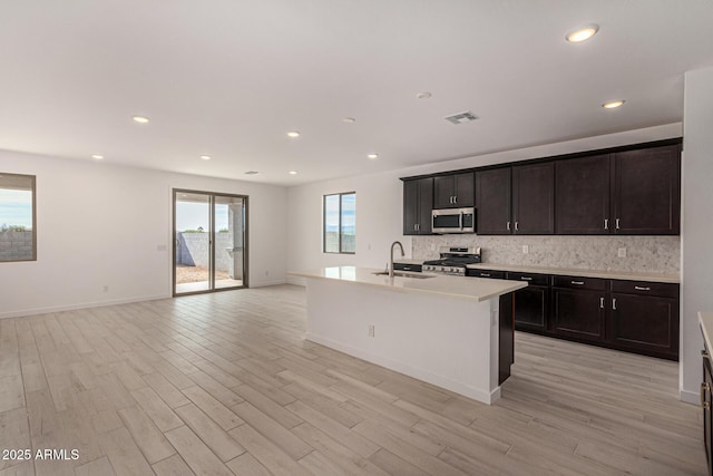 kitchen featuring an island with sink, stainless steel appliances, sink, and light wood-type flooring