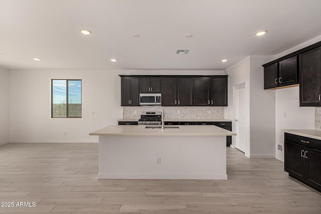 kitchen featuring appliances with stainless steel finishes, tasteful backsplash, sink, a kitchen island with sink, and light hardwood / wood-style floors