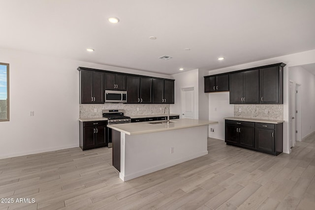 kitchen featuring sink, light hardwood / wood-style floors, an island with sink, and appliances with stainless steel finishes