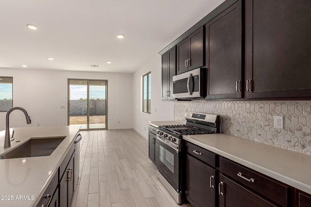 kitchen with sink, dark brown cabinets, stainless steel appliances, tasteful backsplash, and light wood-type flooring