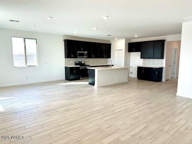 kitchen featuring tasteful backsplash, sink, stainless steel appliances, a center island with sink, and light wood-type flooring