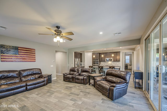 living area featuring a ceiling fan, baseboards, visible vents, and light wood-style floors