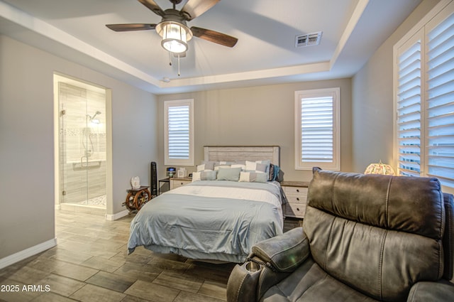 bedroom featuring connected bathroom, wood finish floors, a raised ceiling, baseboards, and visible vents