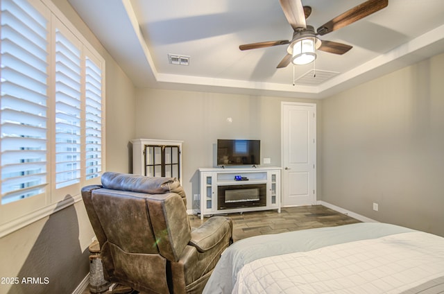 bedroom with a tray ceiling, visible vents, and multiple windows