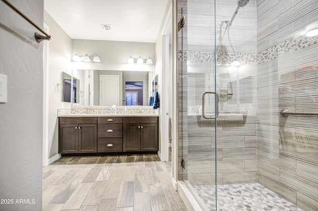 full bath with double vanity, a shower stall, wood finished floors, and visible vents