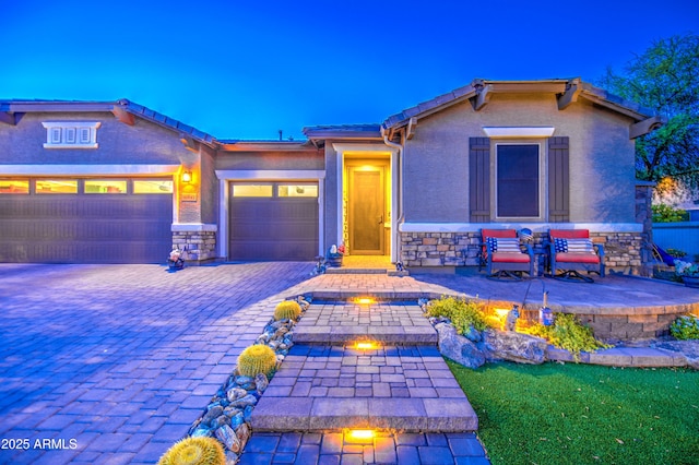 view of front of home featuring decorative driveway, a garage, stone siding, and stucco siding