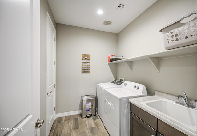 clothes washing area with a sink, washing machine and dryer, light wood-style flooring, and visible vents